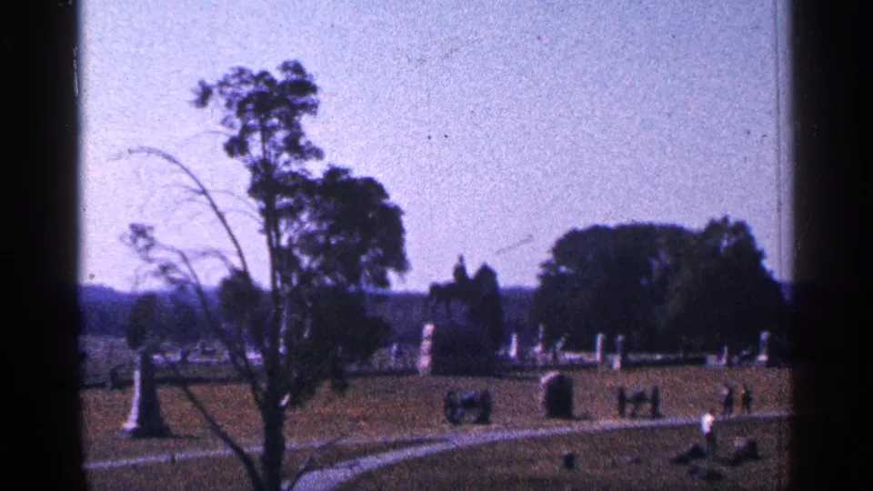 Handheld 1964 8mm view across Gettysburg National Military Park grounds, with monuments, trees, paths, and visitors.