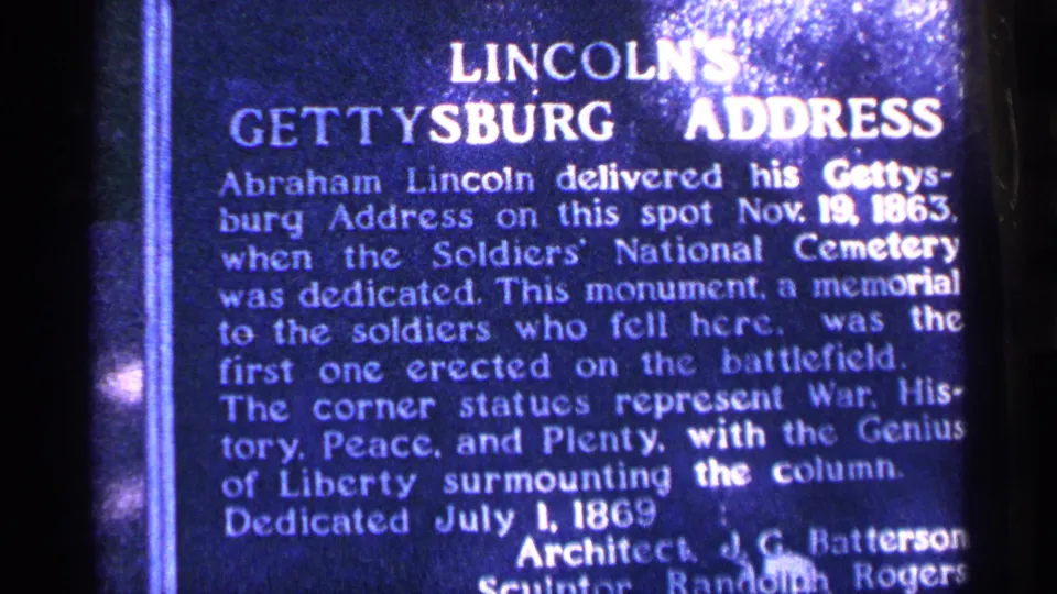 Close 8mm home-movie view of the Gettysburg Address monument plaque in Pennsylvania, with dedication text visible but softened by film grain.
