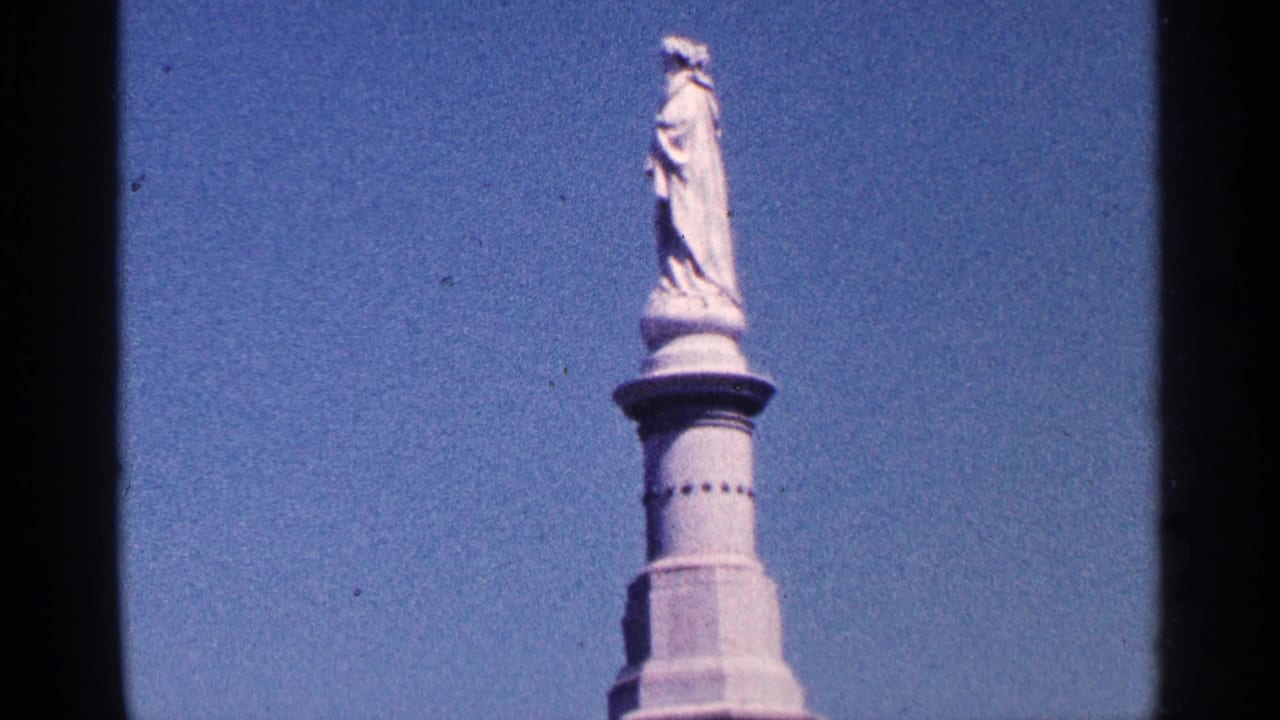 1964 Pennsylvania 8mm frame showing the upper part of a white stone monument with a standing statue against clear blue sky.