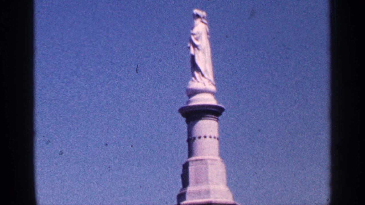 Upper monument with standing statue and column framed by blue sky.