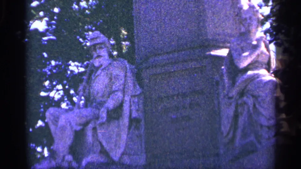 1964 Pennsylvania 8mm frame focused on the monument's carved seated figure and neighboring draped figure, with trees behind them.