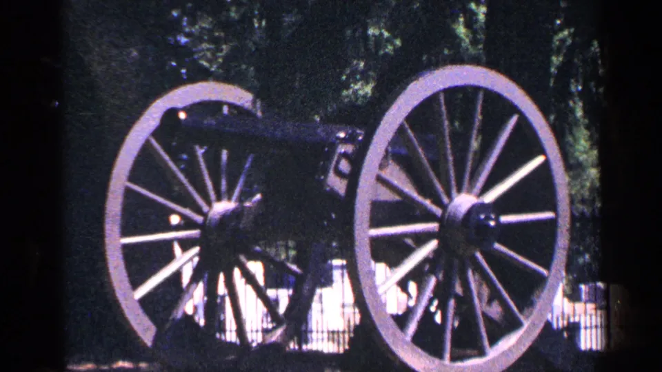 1964 Pennsylvania 8mm close view of a historic cannon display with large spoked wooden wheels, trees behind it, and a low fence in the background.