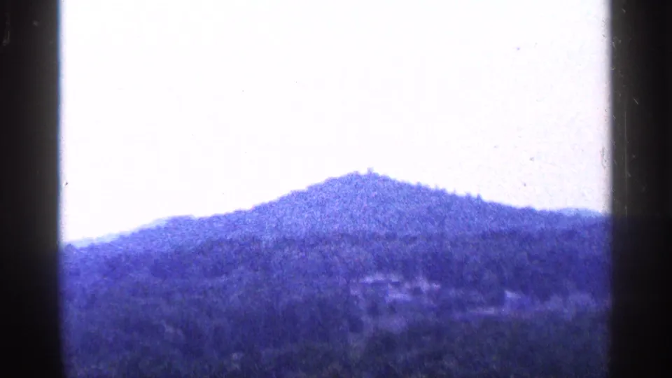 1964 Pennsylvania 8mm frame showing a distant wooded hilltop under a bright pale sky with soft blue-purple film color.