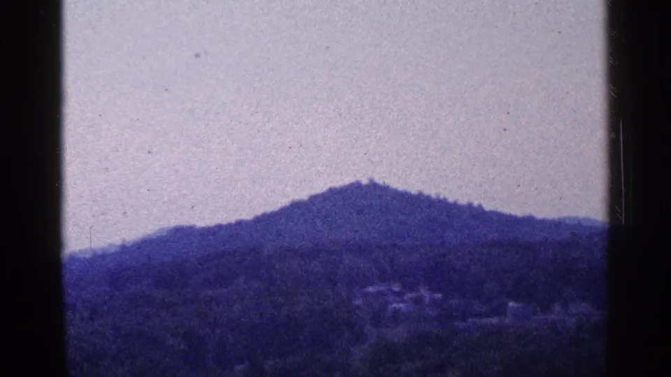 1964 Pennsylvania home-movie frame of a dark wooded hilltop and pale sky, with grain and gate edges visible.