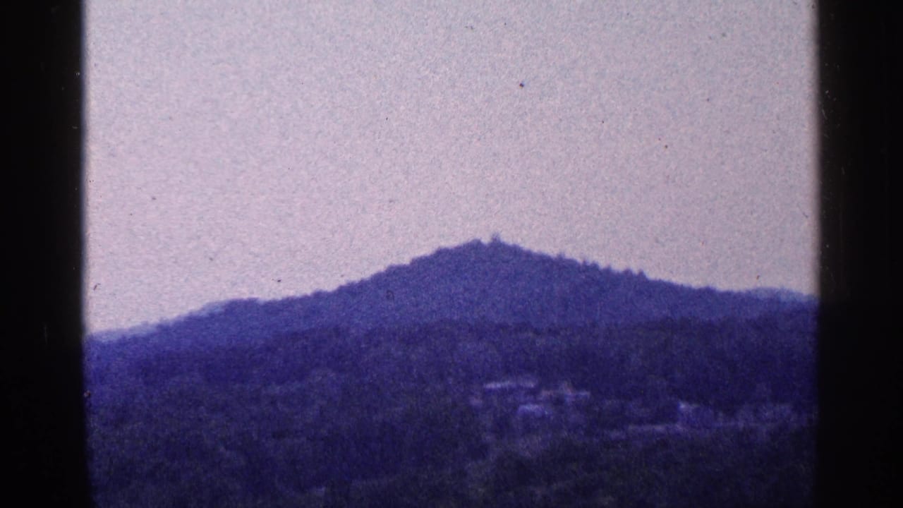 Distant wooded mountain ridge beneath a pale sky on faded 8mm film.