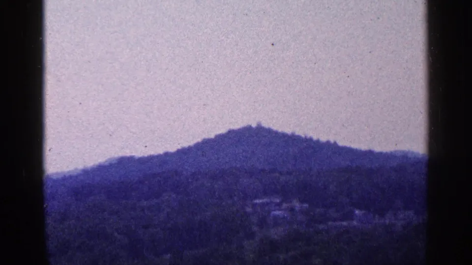 1964 Pennsylvania home-movie frame showing a hazy wooded mountain ridge under a pale sky with visible film gate edges.