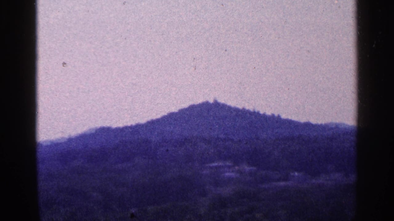 Hazy mountain ridge and wooded hillside framed by dark film borders.