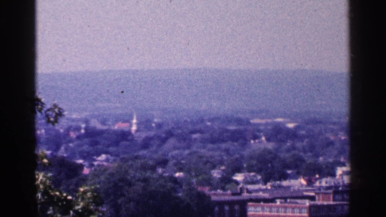1964 Pennsylvania view over a town, with a white church steeple rising among trees and hills.