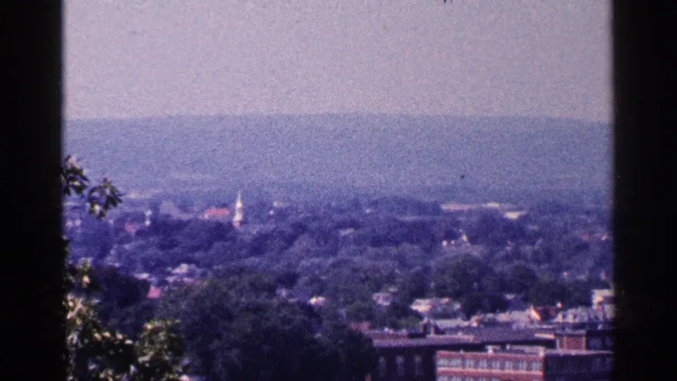 1964 Pennsylvania 8mm frame with a soft, hazy view of town buildings, trees, and a distant steeple.
