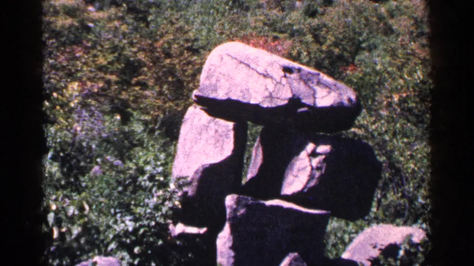 1964 Pennsylvania home-movie frame showing an unusual stacked boulder formation amid dense greenery.