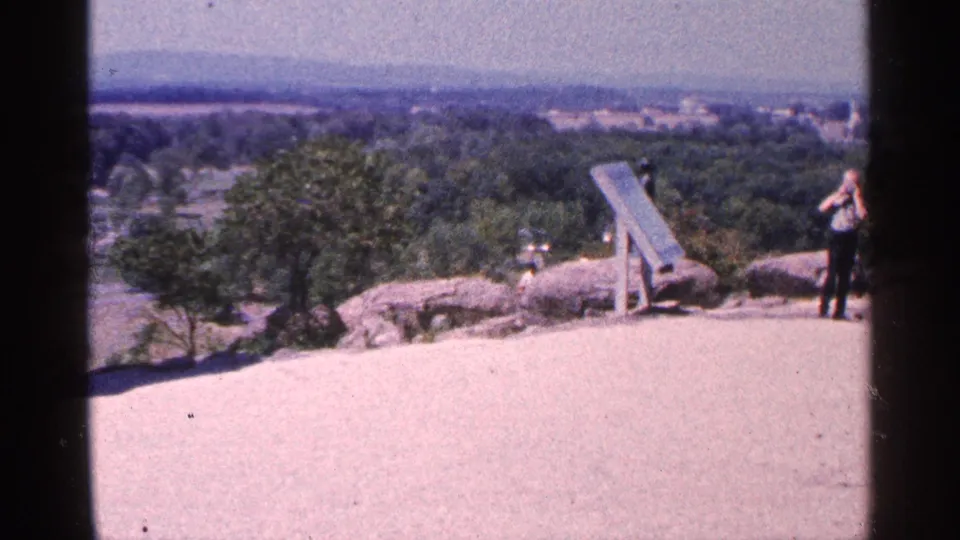 Final frame of the Pennsylvania overlook view, with rocks, trees, a wooden fixture, distant hills, and a partially framed person at right.