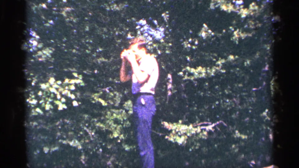 A person in blue clothing stands in a wooded Pennsylvania setting in 1964, holding binoculars up while facing the trees.