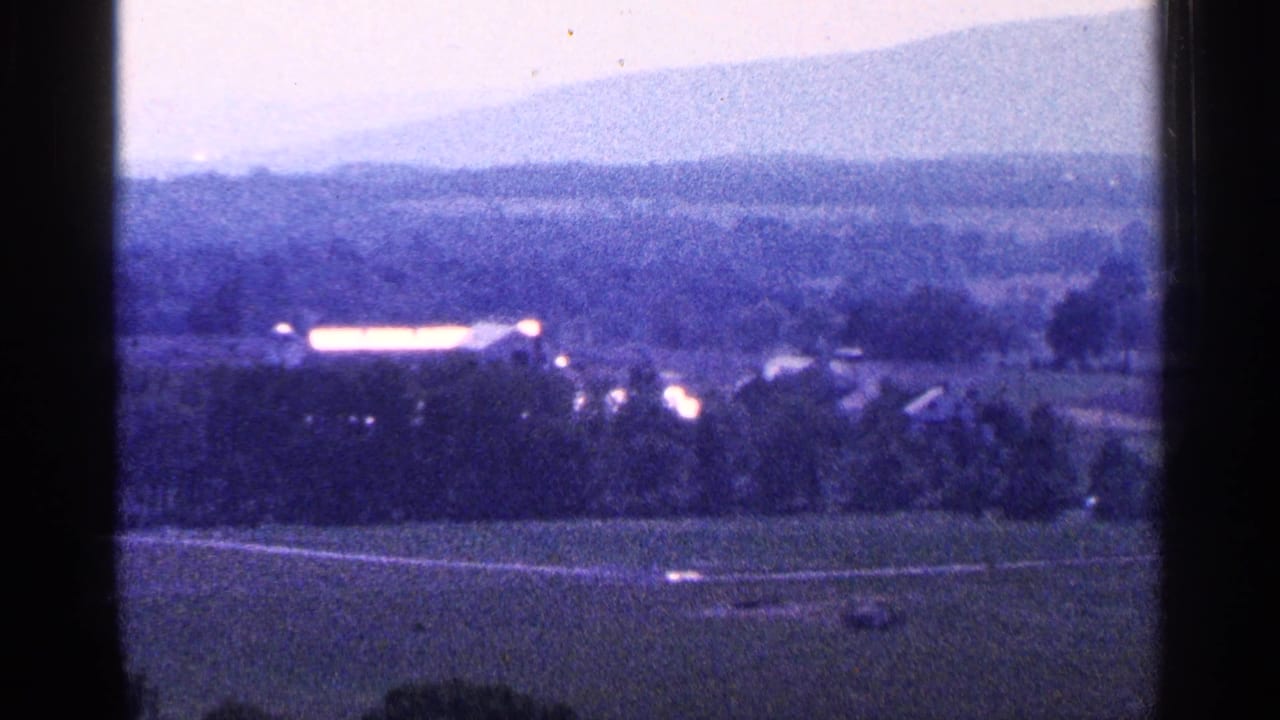 1964 Pennsylvania 8mm frame looking over farmland and scattered buildings toward a hazy mountain silhouette.