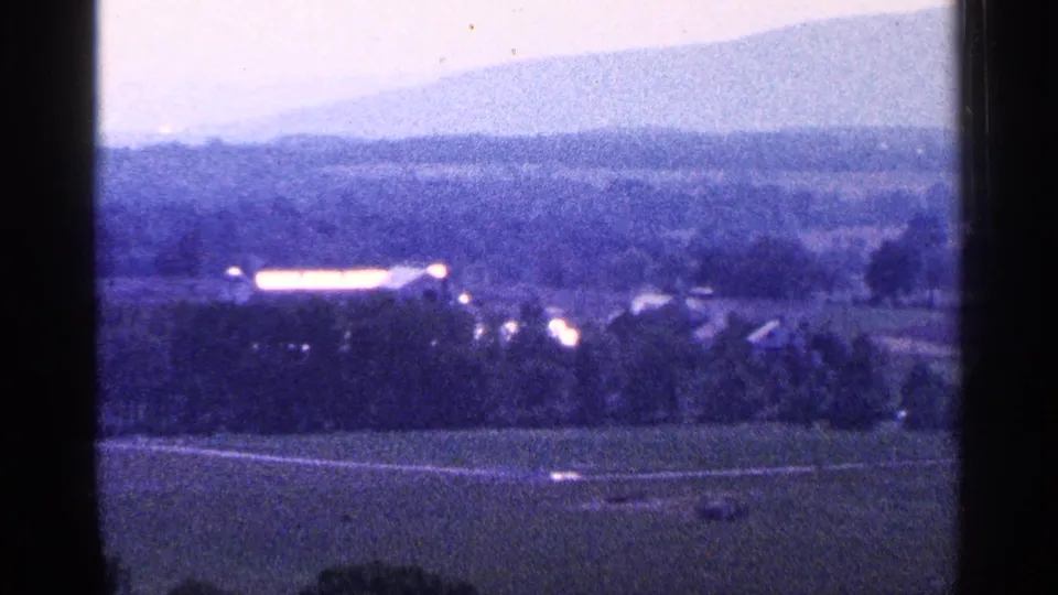 1964 Pennsylvania 8mm frame looking over farmland and scattered buildings toward a hazy mountain silhouette.