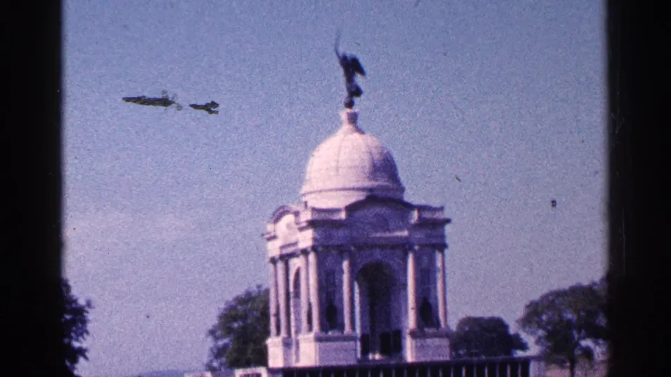 The camera shifts toward the domed Gettysburg memorial structure, with a statue silhouette on top, trees below, and visible 8mm film marks.