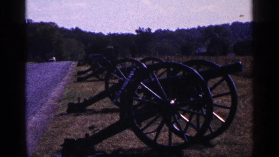 1964 Pennsylvania 8mm frame showing dark historic cannons on a grassy field near a path and tree line.