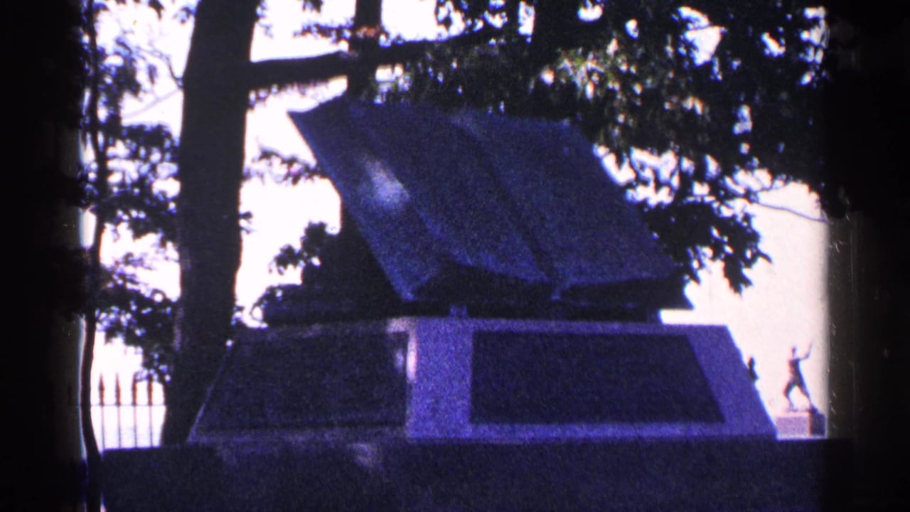 Open book monument seen through trees with fence spikes at left.