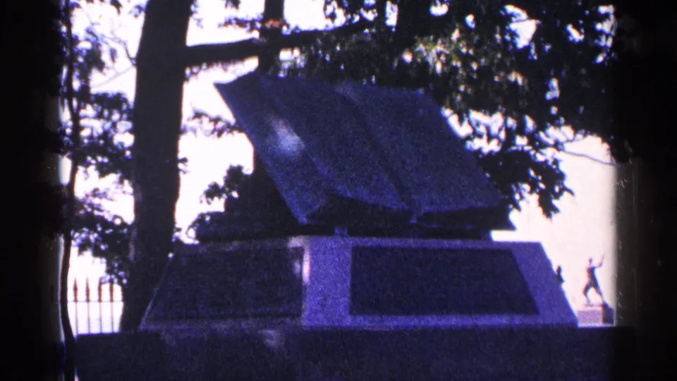 Visitor-shot 1964 Pennsylvania frame of an open book-style monument, partly obscured by trees and dark film borders.