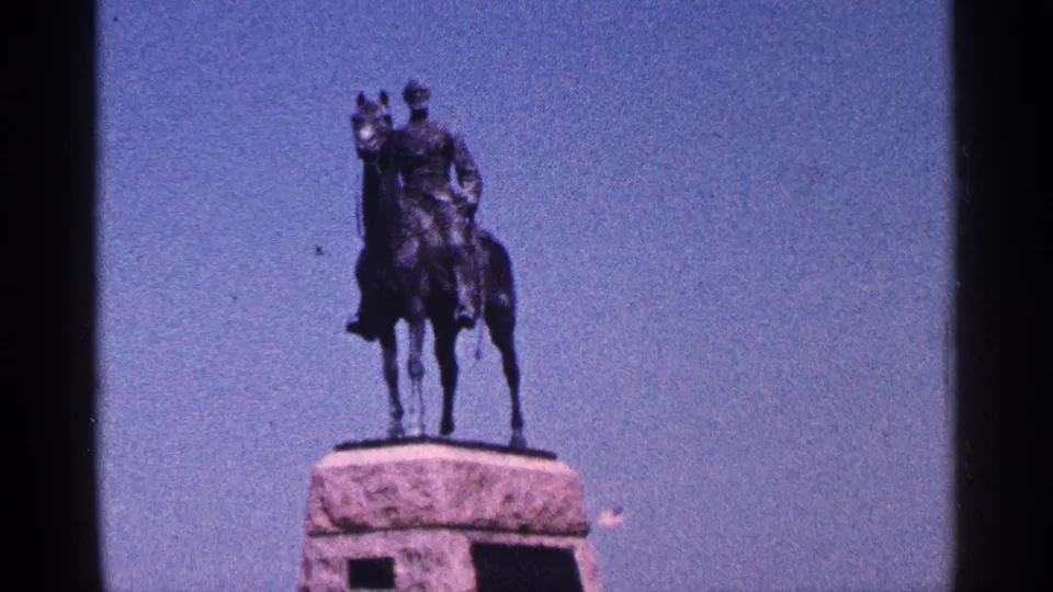 1964 Pennsylvania 8mm frame showing a man on horseback statue mounted on a stone pedestal beneath a clear blue sky.