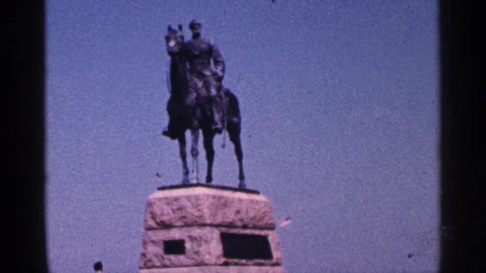 1964 Pennsylvania home-movie frame of an equestrian monument with a rider figure on a tall stone pedestal.