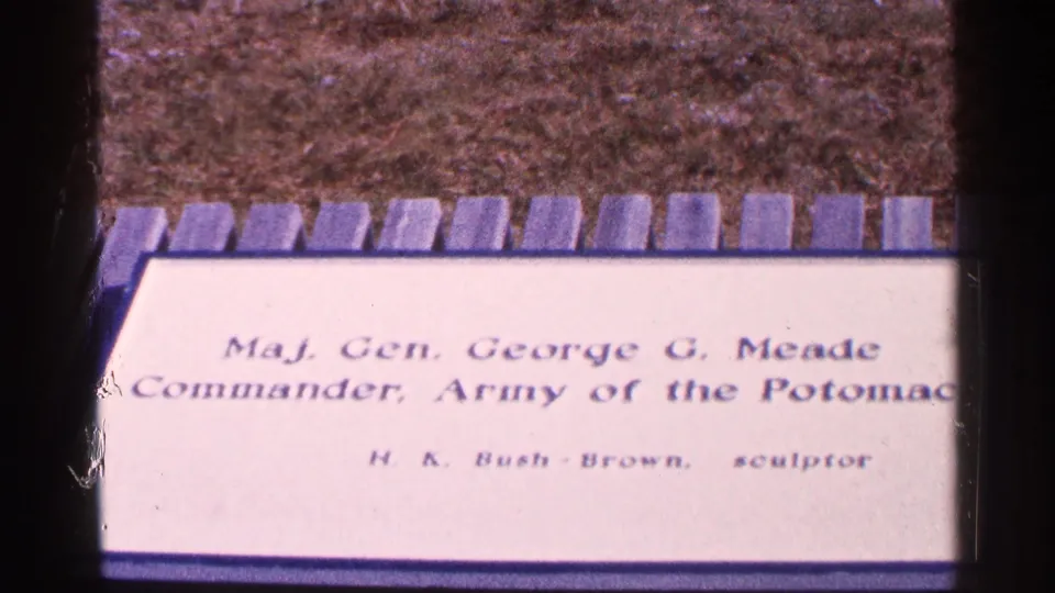 1964 home-movie frame with the Meade memorial plaque centered, showing the commander title and sculptor credit amid visible film borders.