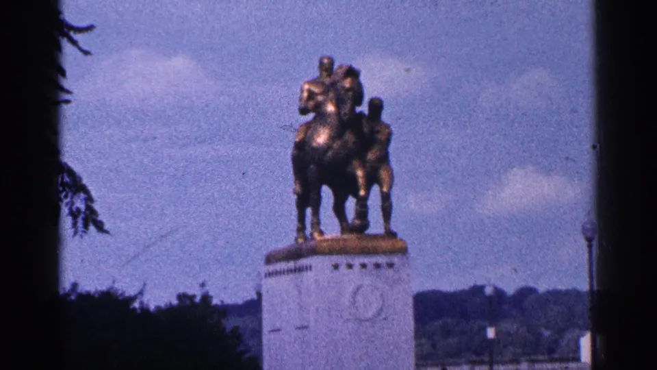1964 Washington, D.C. home-movie frame showing a bronze equestrian statue on a stone pedestal in a public setting.