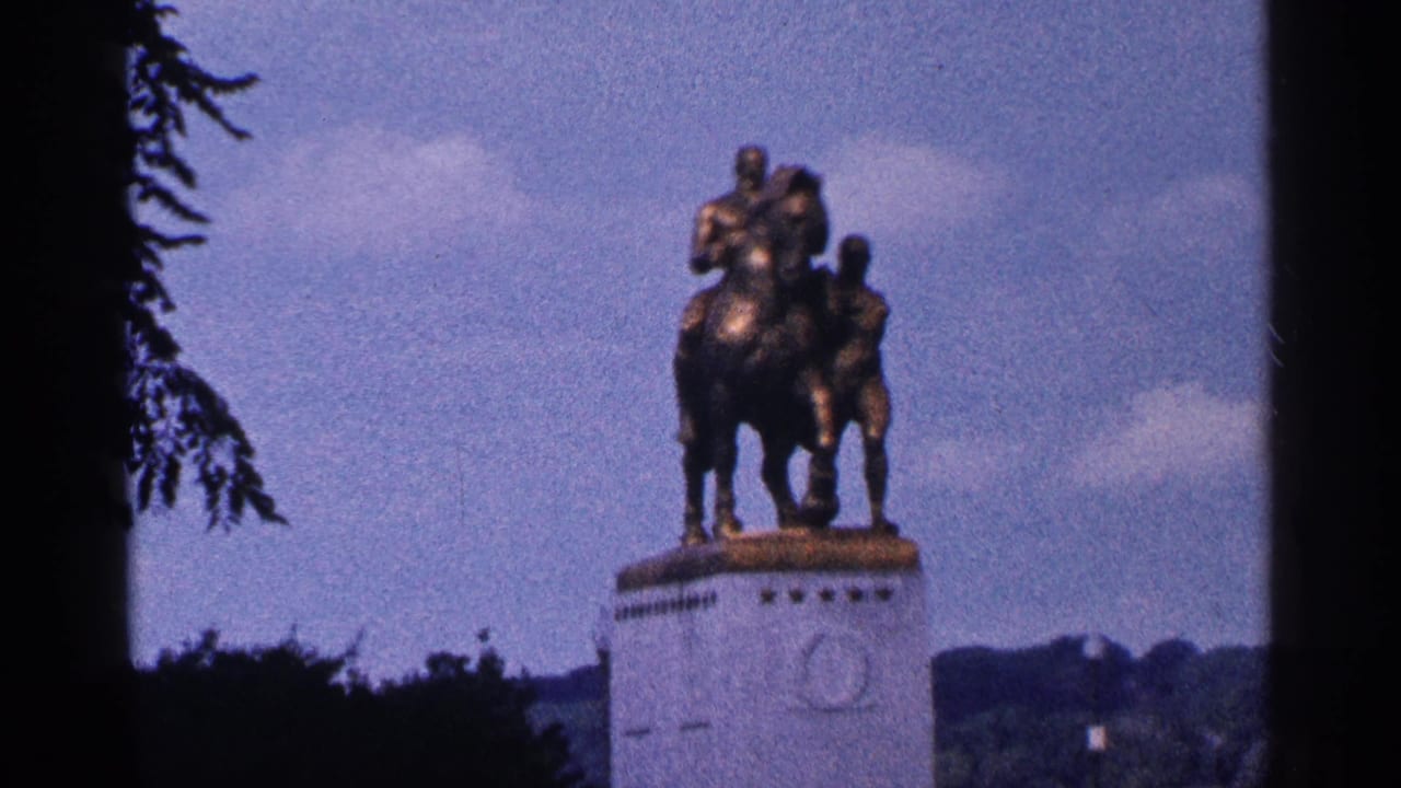 Horse-and-rider monument on a pedestal with trees and sky behind it.