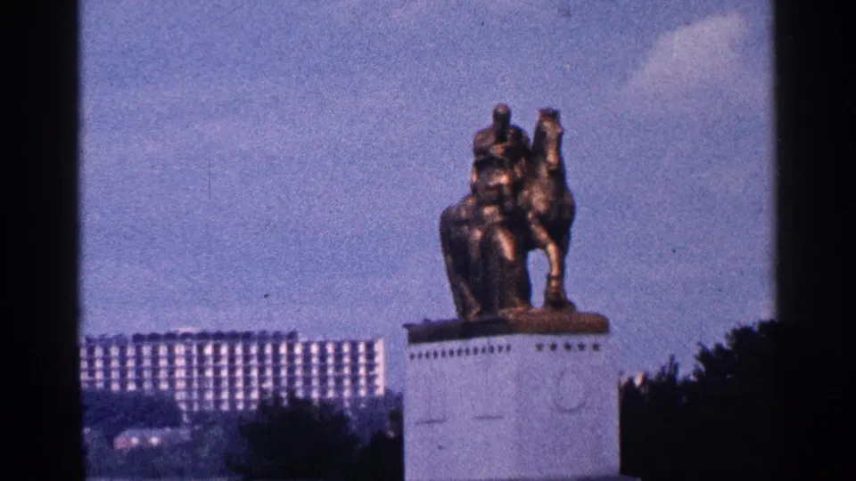 1964 Washington DC frame showing the monument from another angle, with a rectangular building, lamppost, trees, and sky in the background.