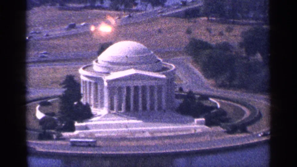 1964 8mm aerial view of the Jefferson Memorial in Washington DC beside the Tidal Basin, with trees, roads, and small vehicles visible.