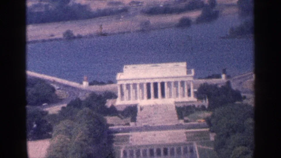 1964 Washington, DC aerial home-movie frame showing the Lincoln Memorial, adjacent water, trees, and nearby roads.