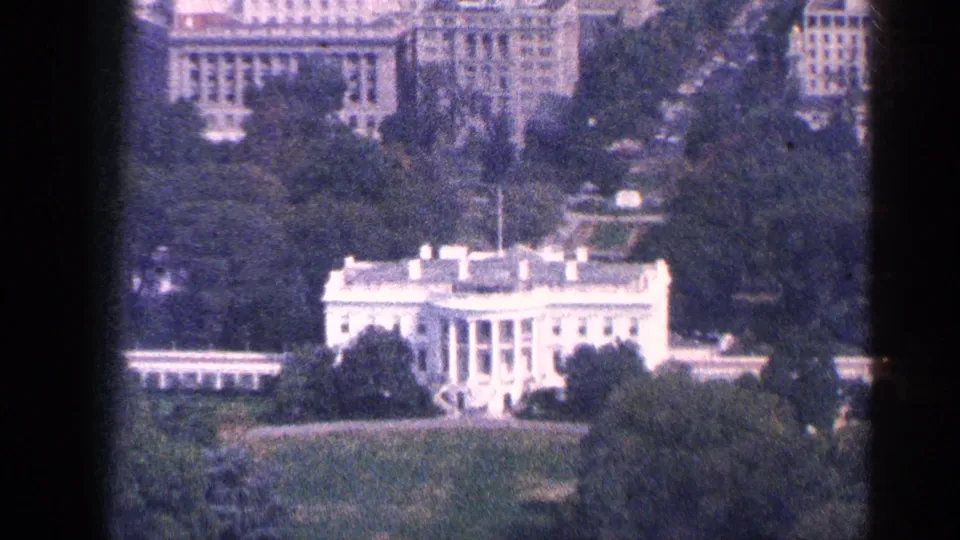 Washington, DC aerial home-movie frame from 1964 showing the White House, green lawn, trees, and surrounding urban architecture.