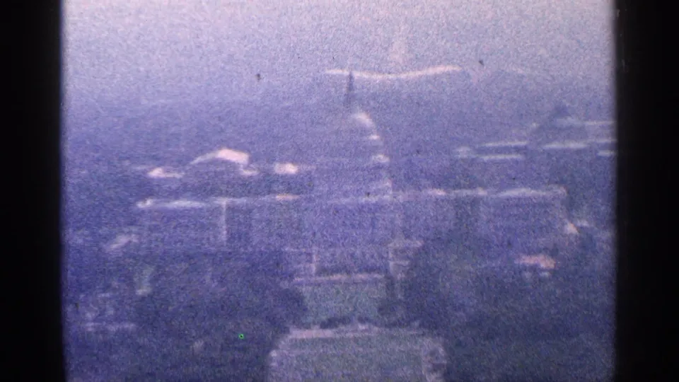 1964 Washington, DC home-movie frame with a soft, blue-tinted distant view of the U.S. Capitol dome and nearby city structures.
