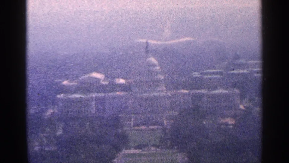 1964 Washington, DC frame showing the U.S. Capitol dome through heavy haze, with trees and low city buildings softened by the 8mm film image.