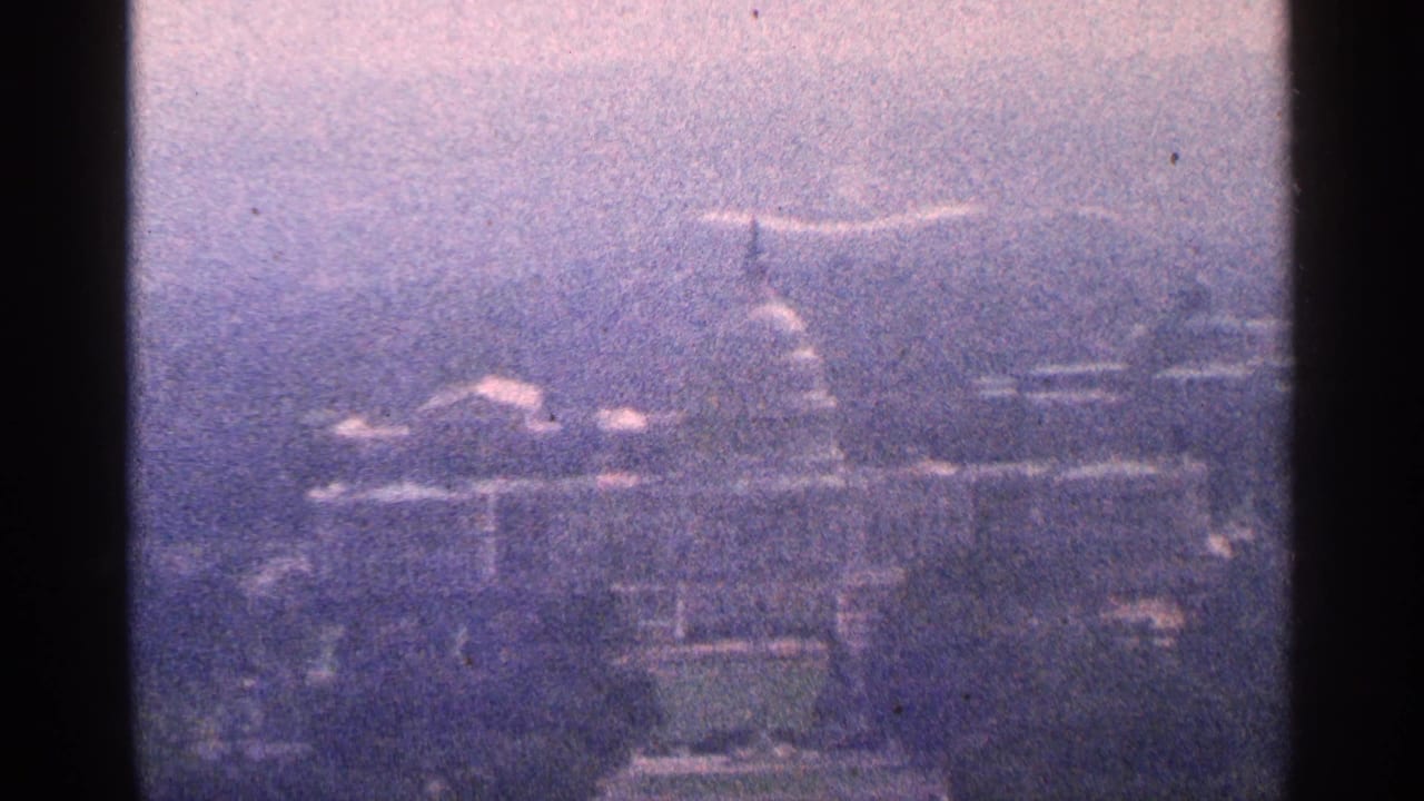 Hazy 1964 8mm home-movie view toward the U.S. Capitol in Washington, D.C., with the dome faintly visible through atmospheric softness.