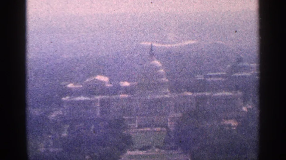 Hazy 1964 8mm home-movie view toward the U.S. Capitol in Washington, D.C., with the dome faintly visible through atmospheric softness.
