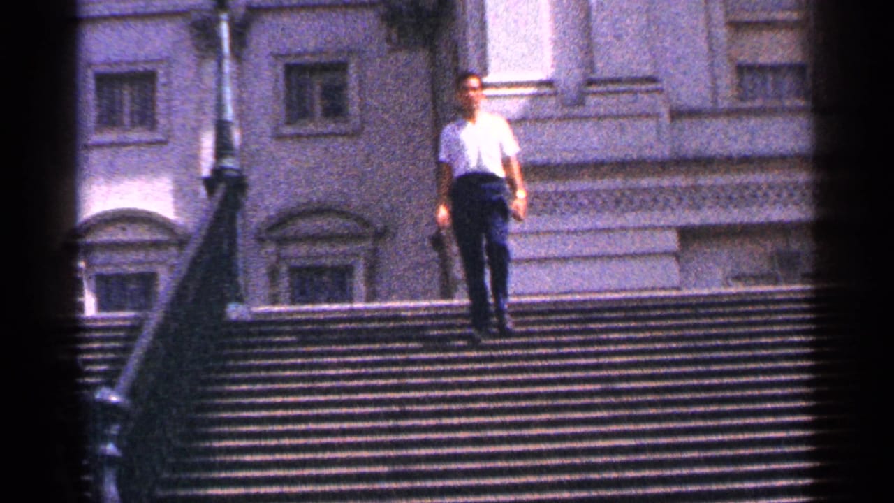 Man in a white shirt walking down a wide outdoor staircase beside metal railings.