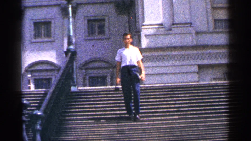 An adult man descends the wide Washington DC steps, holding a small object as the 8mm frame softens the facade behind him.