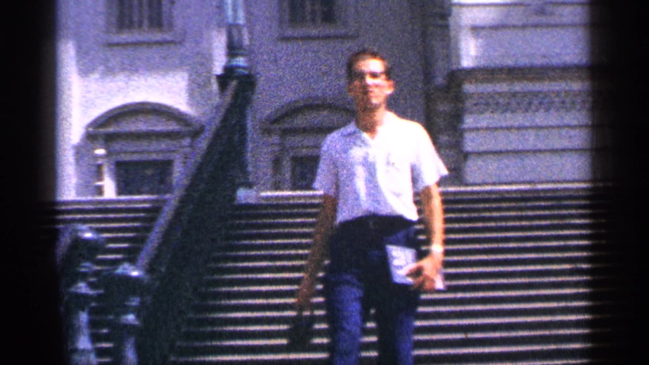 Man in a white shirt walking down broad stone steps in front of a classical building.