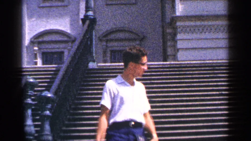 A profile view shows the man moving across the Capitol steps, with the stone facade and dark stair railing behind him.