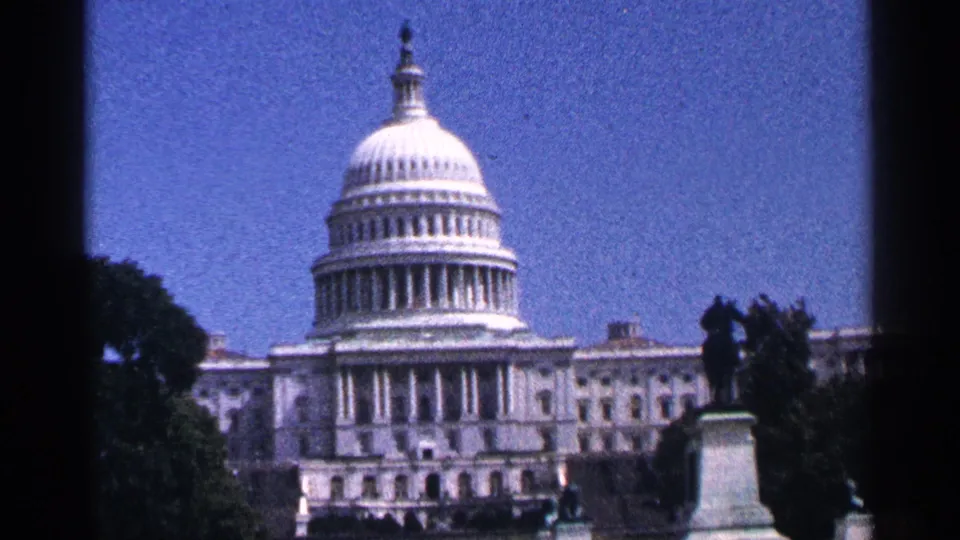 The U.S. Capitol dome appears in a distant 1964 Washington, DC view, with trees, a statue, and blue sky in the frame.