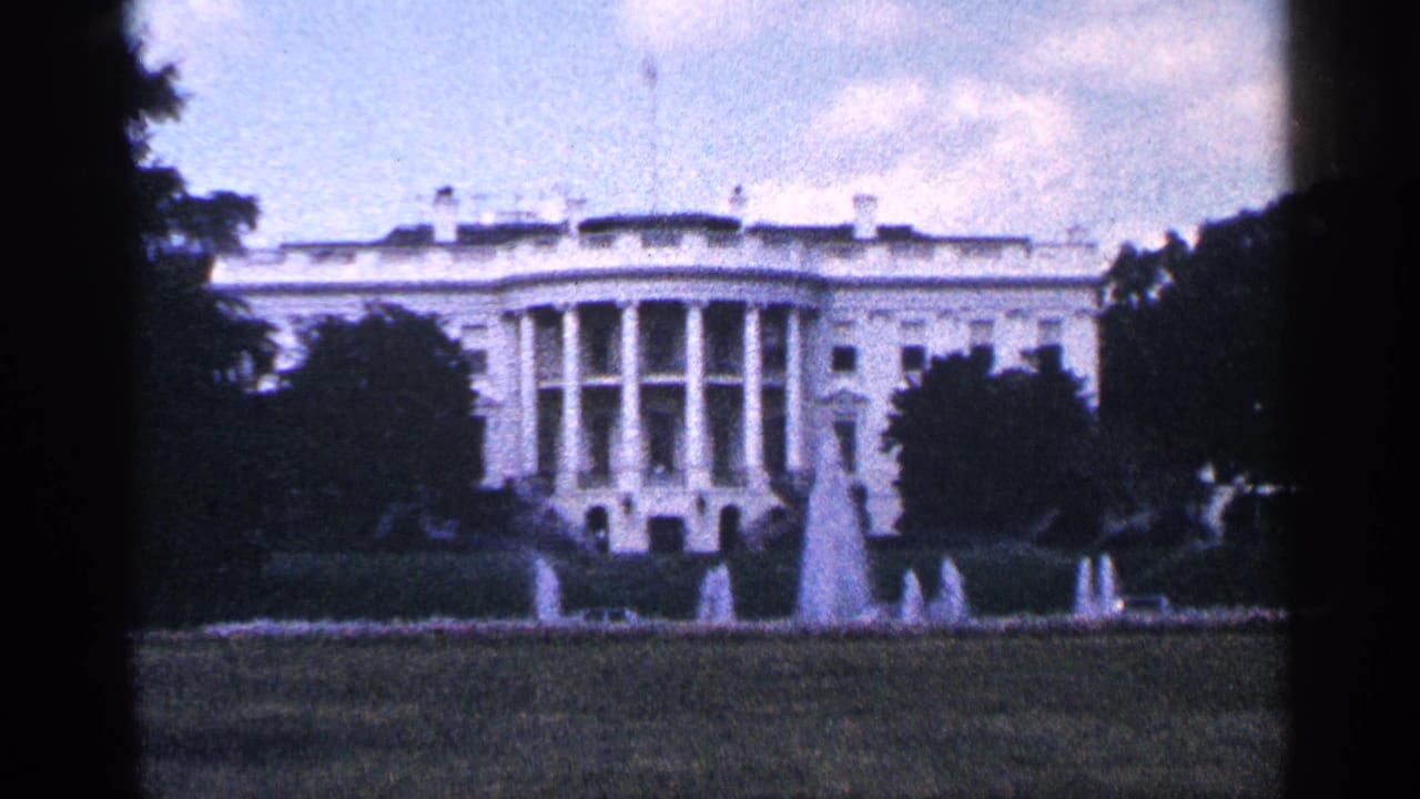 1964 8mm view of the White House in Washington, DC, framed by lawn, trees, fountains, and dark film-edge borders.