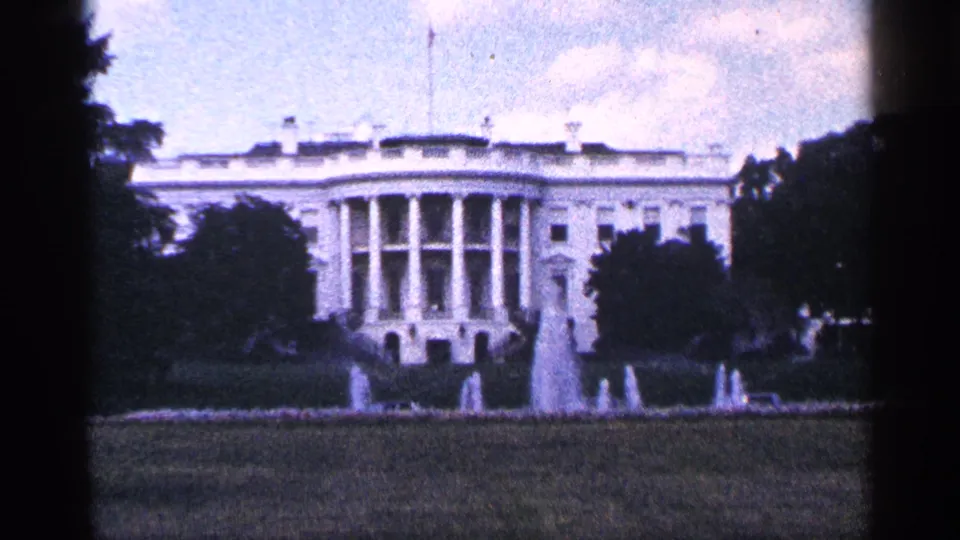 Visitor-shot 1964 view of the White House exterior across the grounds, with fountains active and trees partly framing the building.