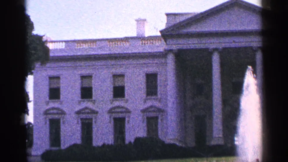 Closer 1964 8mm frame of the White House exterior in Washington, DC, showing windows, portico columns, hedges, and fountain spray.
