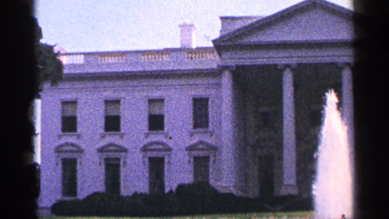 1964 8mm view of the White House facade in Washington, DC, with a foreground fountain and soft tree framing.