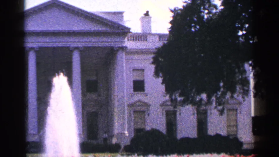 1964 Washington, DC home-movie frame showing the White House portico, fountain spray, shrubs, and right-side tree canopy.