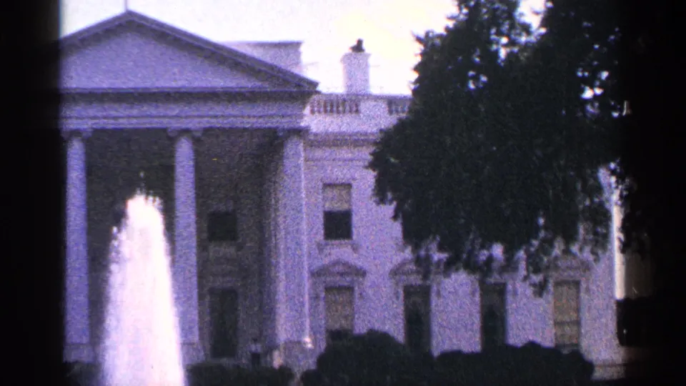 1964 8mm frame of the White House exterior with fountain plume at left and a large tree covering part of the facade.