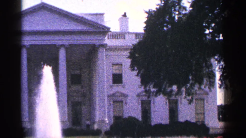 1964 Washington, DC 8mm frame with the White House facade, fountain spray, shrubs, and heavy tree coverage on the right.