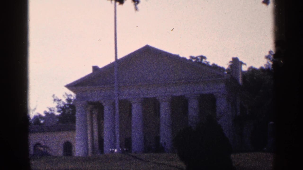 Columned house and flagpole seen through dark film edges and trees.