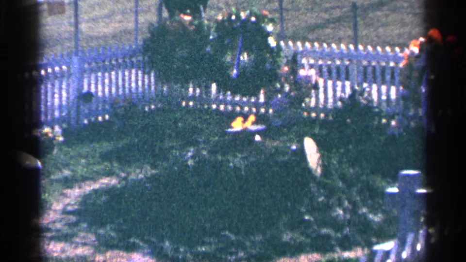 1964 Washington, DC visitor-film view of a bright eternal flame near a wreath and white fence, with soft focus and heavy grain.