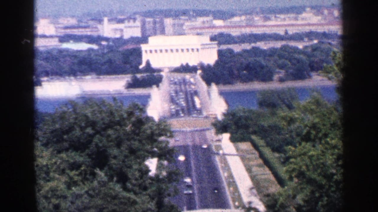 High-angle view toward the Lincoln Memorial, reflecting water, road traffic, trees, and distant buildings.